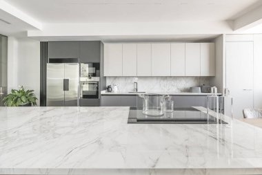 Beyaz mermer adalı modern mutfak, entegre paslanmaz çelik aletler, ve kabin altı LED ışıklandırma