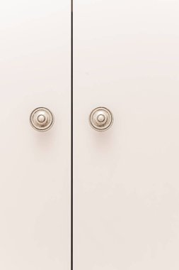 İki uzun, pürüzsüz gardırop kapısı parlak beyaz kaplamalı büyük, belirgin, yuvarlak, gümüş paslanmaz çelik kulplu, tasarıma endüstriyel ve işlevsel bir dokunuş ekliyor.