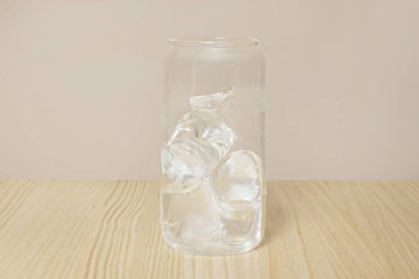 Açık ahşap bir masada buzla dolu berrak bir bardak.