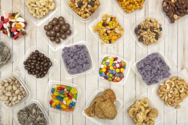 Mor ve kahverengi tonlarında bir kompozisyon, mor renkli şekerlerin yanında kurumuş kızılcıklarla dolu mor bir plastik kase ve kabuklu ceviz gösteriyor.