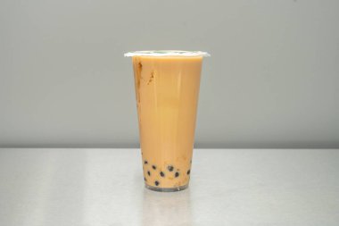 Bir bardağın dibine istiflenmiş parlak siyah tapyoka incilerinin aşırı yakın çekimi, Tayland sütlü çayının kehribar sıvısının içinden görülüyor.