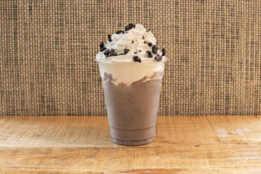 Uzun bir bardakta servis edilen kalın, soğuk bir çikolatalı milkshake, üzerine bol miktarda krema dökülmüş, kenarlardan nazikçe dökülen..
