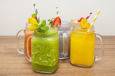 İçinde yeşil kivi tabanı, sarı mango tabakası, turuncu havuç ve turuncu üst katman bulunan katmanlı cam bir sürahi..