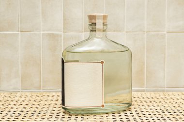 Renksiz bir sıvı içeren temiz bir cam şişenin minimalist çizgileri, her bir tipografik etiketi vurgulayan serin, gevrek bir ışık ile dokulu gri bir arkaplan üzerinde yakalanır..