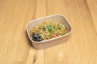 Geniş Çin erişteleri, et şeritleri ve brokoliyle dolu, karton kapağıyla mühürlenmeye hazır bir paket servis konteynırı..