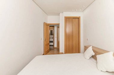 Modern bir süit yatak odası, açık bir soyunma odasını özel tasarım elbise askıları ve cam raflarla donatıyor. Görsel olarak uyuma alanından aydınlık ve zarif bir ahşap ekran ile ayrılmış.