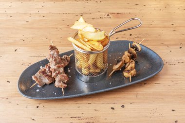 Dumanlı aromaların ve dokuların mükemmel bir kombinasyonu. Karakteristik karamelize pırıltılarıyla marine edilmiş domuz şişleri ince patates kızartmaları ve serpilmiş kağıt koni üzerinde servis ediliyor.