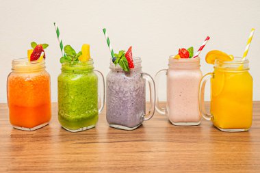 Güneşli bir tezgahın üzerine dizilmiş beş kavanozdan oluşan bir grup, turuncu, çilek pembesi, ananas sarısı ve ıspanak yeşili içeren kromatik bir meyve çeşitliliği sergiliyorlar.