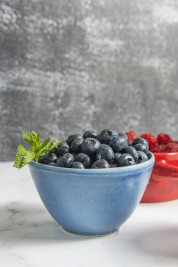 Açık renkli bir yüzeyde cam bir kabın üzerine yerleştirilmiş ince ağlı metal süzgecin içindeki yaban mersinli bir sahne.