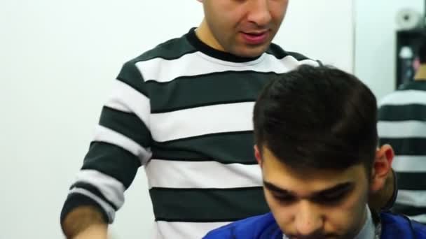 Парикмахер сокращает волосы мальчика электрическим клиппером и ножницами — стоковое видео