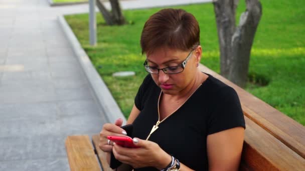 Mujer joven en gafas hablando en el teléfono móvil en un parque de la ciudad . — Vídeo de stock