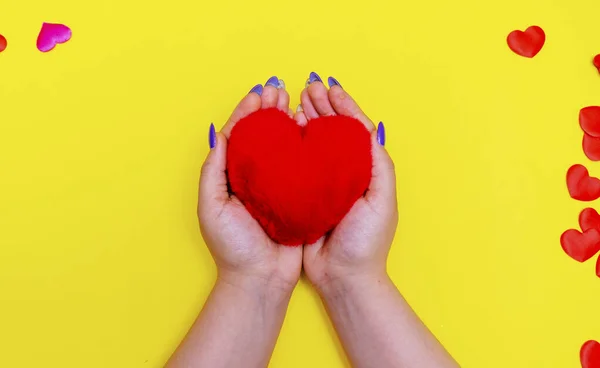 Red heart is a symbol of love in the hands of a girl on a yellow background. Valentine\'s Day. The view from the top