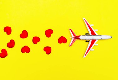 Uçak oyuncağı ve kalp sarı arka planda, aşk yolculuğu konsepti.