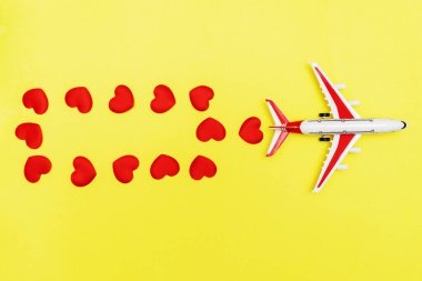 Uçak oyuncağı ve kalp sarı arka planda, aşk yolculuğu konsepti.
