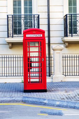 Geleneksel bir İngiliz kırmızı telefon kulübesi sokakta duruyor..