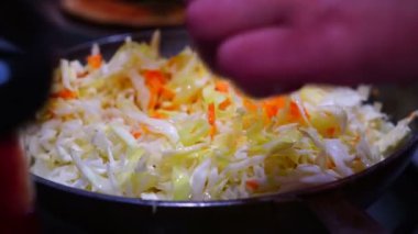 Kadın tavada haşlanmış lahana ve havuç pişiriyor.