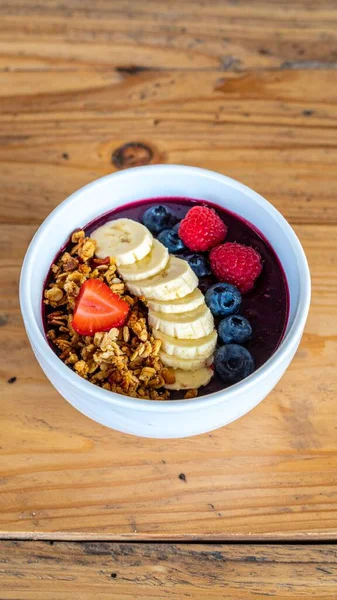 Taze Böğürtlen, Muz ve Granola ile Acai Bowl En İyi Tatlı Nesnesi ve Superfood Konsepti için Tahta Masa üzerinde sunuldu