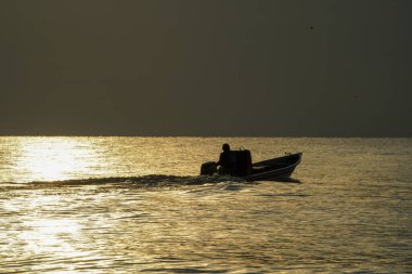 Güneşin doğuşunda ya da batışında altın parıldayan denizde küçük bir teknede bir balıkçının silueti..