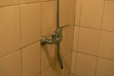 Chrome Shower Faucet On Beige Tiled Wall With Water Droplets Close Up Warm Lighting