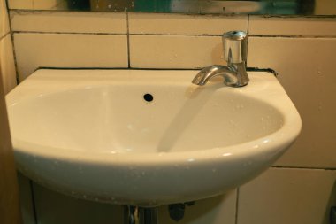 White Ceramic Sink With Chrome Faucet Covered In Water Droplets In A Tiled Bathroom