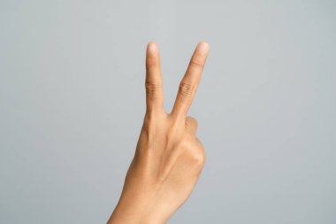 Bir elin yakın çekimi, iki parmağının gri bir arka plana doğru yükseldiğini gösteriyor.