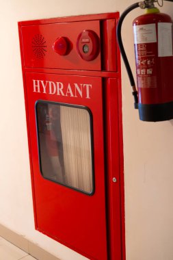 Kırmızı metal yangın söndürme musluğu beyaz bir duvara monte edildi ve yangın söndürücü takıldı.