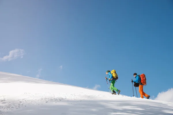 Twee wandelaars tegen blauwe hemel in winter bergen. — Stockfoto