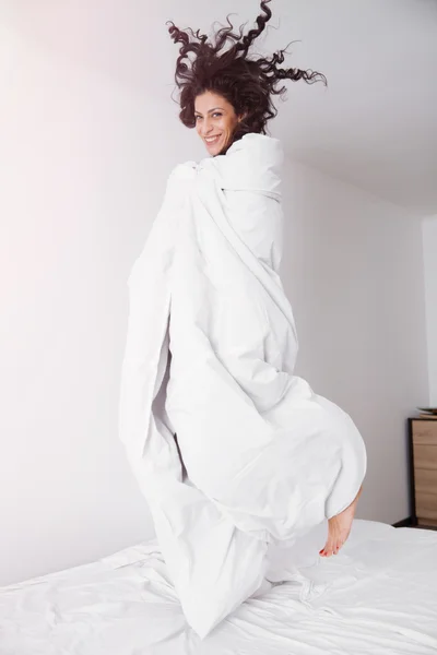 Esmer kadın beyaz yatakta atlama — Stok fotoğraf