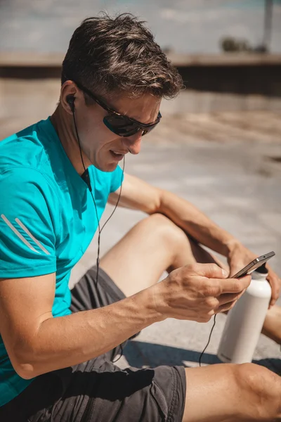 Atleta descansando con smartphone después de correr por la ciudad — Foto de Stock