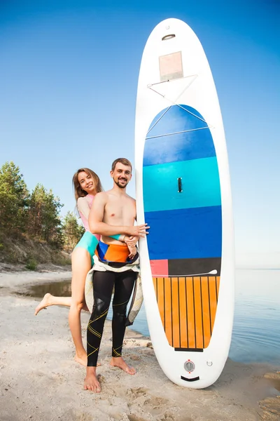 Junges Paar mit Surfbrett am Strand — Stockfoto