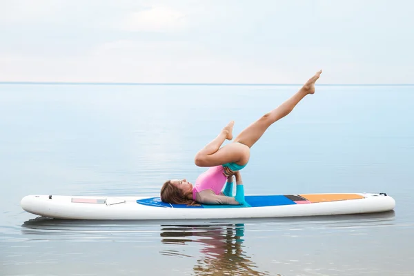 Vrouw doet yoga op board van sup met peddel — Stockfoto