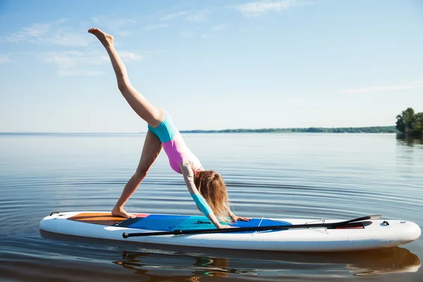 Woman doing yoga on sup board with paddle