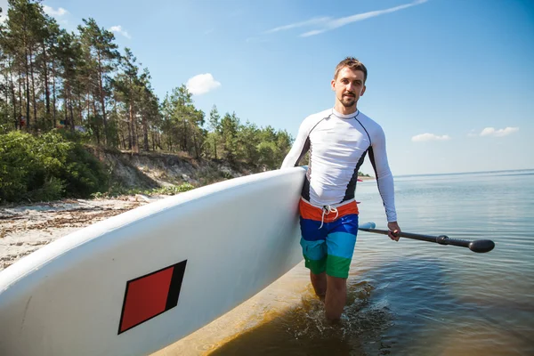 Młody człowiek z pokładzie wiosła na plaży — Zdjęcie stockowe