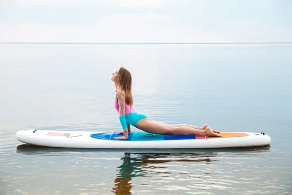 Frau macht Yoga auf Surfbrett mit Paddel — Stockfoto