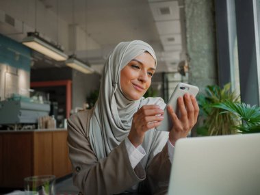 Kafede uzaktan eğitim, çevrimiçi eğitim veya video sohbeti yapan Müslüman kadın