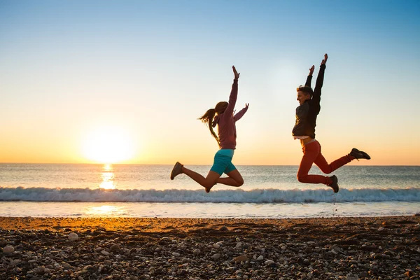 Couple jumps on the beach over sunrise — Stock Photo, Image