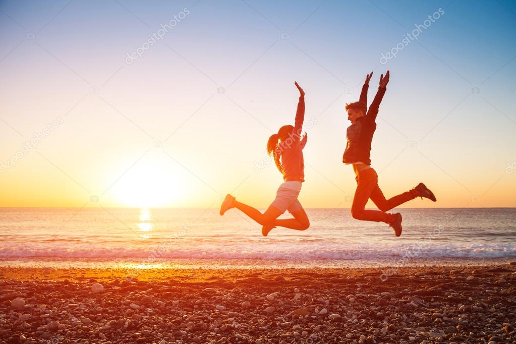 Couple jumps on the beach over sunrise