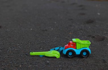 İspanya 'nın Kanarya Adaları' ndaki Tenerife sahilinde siyah volkanik kumun üzerinde duran yeşil kürekli parlak bir plastik damperli kamyonun panoramik görüntüsü.