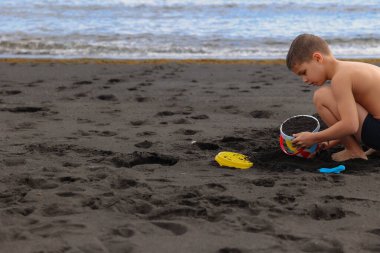 İspanya 'nın Tenerife Kanarya Adaları' ndaki siyah bir volkanik plajda diz çökmüş genç bir çocuğun gizli görüntüsü..