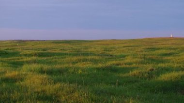 Göl kenarındaki bir tepenin tepesinde uzun bir çimen tarlası. Güzel günbatımı renkleri ve gökyüzünde ve çayırda parlayan.