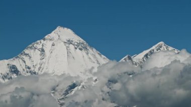 Zaman bulutları bir dağ vadisinde kıvrılır. Uzakta karlı bir tepe. Mustang, Nepal, Annapurna