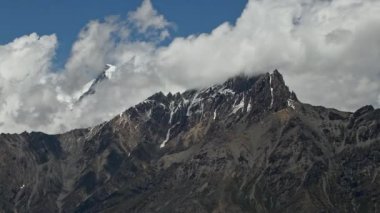 Zaman bulutları bir dağ vadisinde kıvrılır. Uzakta karlı bir tepe. Mustang, Nepal, Annapurna