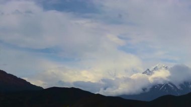 Zaman bulutları bir dağ vadisinde kıvrılır. Uzakta karlı bir tepe. Mustang, Nepal, Annapurna