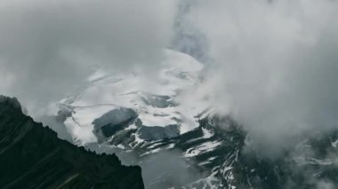 Zaman bulutları bir dağ vadisinde kıvrılır. Uzakta karlı bir tepe. Mustang, Nepal, Annapurna