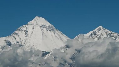 Zaman bulutları bir dağ vadisinde kıvrılır. Uzakta karlı bir tepe. Mustang, Nepal, Annapurna