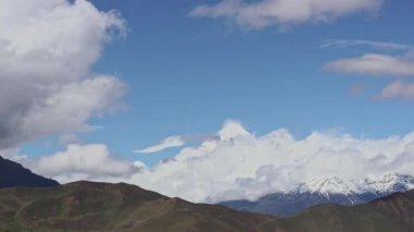 Zaman bulutları bir dağ vadisinde kıvrılır. Uzakta karlı bir tepe. Mustang, Nepal, Annapurna