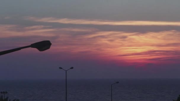 Tijdsverloop. Oranje zonsondergang boven de zee. Het uitzicht vanuit het huis, met lantaarnpalen die oplichten in het donker. — Stockvideo