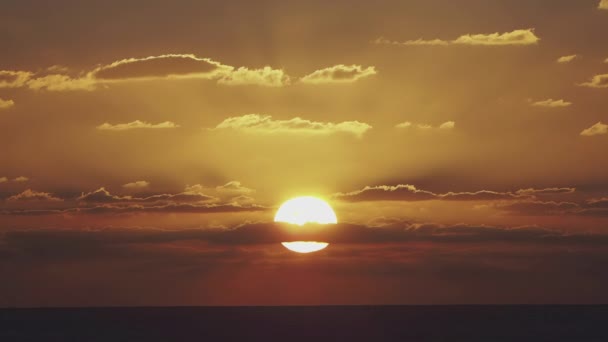 Bright disk of sun moves through gapes of clouds in shining sunset sky — Stock Video