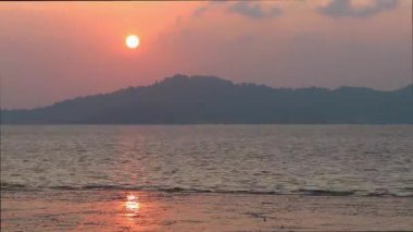 Sakin bir denizin kıyısında Pembe Gün batımı, Güneş dağın arkasında batar.