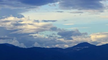 Zaman bulutları mavi dağların üzerinde kıvrılır, uzaktaki karlı zirve.